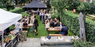 BBQ-Catering-Empfang im Garten mit Gästen an langen Tafeln und Grillstation unter schwarzem Pavillon @ 