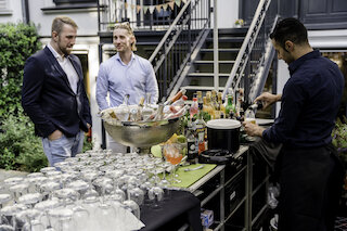 Zwei Gäste an einer mobilen Cocktailbar beim BBQ-Catering während der Barkeeper Getränke mischt @ 