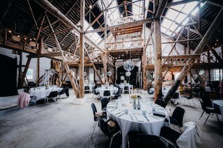 Rund gedeckte Festtafeln mit weißen Tischdecken in einer Halle mit historischem Holzbindwerk @ 